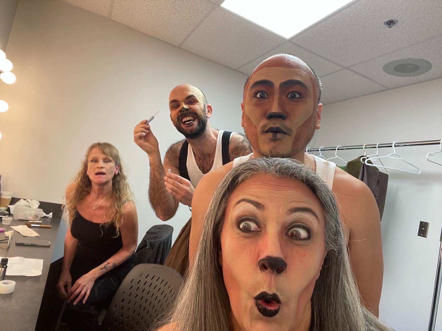 Four actors group together facing the camera. They are in the dressing room and they are putting on makeup to make them look more like animals